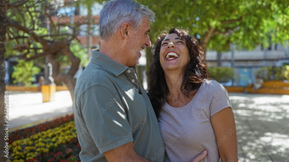 Middle aged couple laughing together outside in a sunny park setting, surrounded by green trees and colorful flowers, expressing happiness and love. Middle aged couple laughing together outside in a sunny park setting, surrounded by green trees and colorful flowers, expressing happiness and love.