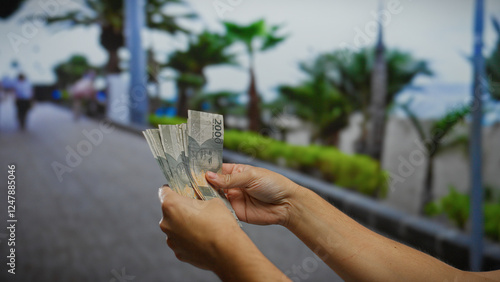 Man holding indonesian rupiah banknotes on an urban street with blurred city backdrop symbolizing financial transactions and business activities outdoors. photo