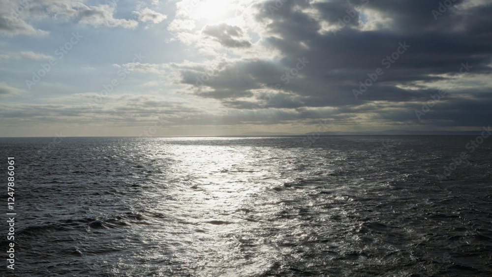 Fototapeta premium Ocean reflecting sunlight under a cloudy sky with horizon visible in the distance, creating a dramatic and serene seascape in a natural outdoor setting.