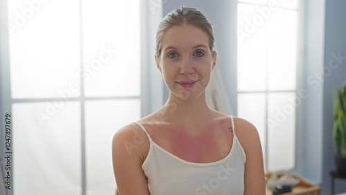 Young blonde woman at a beauty spa center with a sunburn on her shoulders, standing indoors in front of large windows, looking relaxed and content Free Download Young blonde woman at a beauty spa center with a sunburn on her shoulders, standing indoors in front of large windows, looking relaxed and content - GFXLoad
