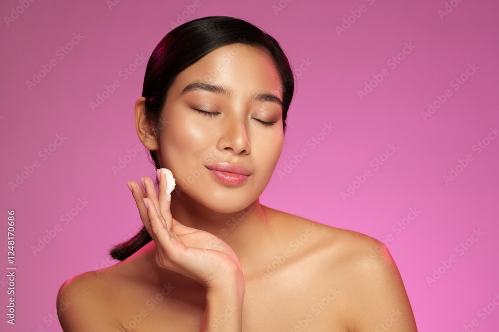 Glowing skin routine with a woman applying cream in a bright studio setting with pink background Glowing skin routine with a woman applying cream in a bright studio setting with pink background