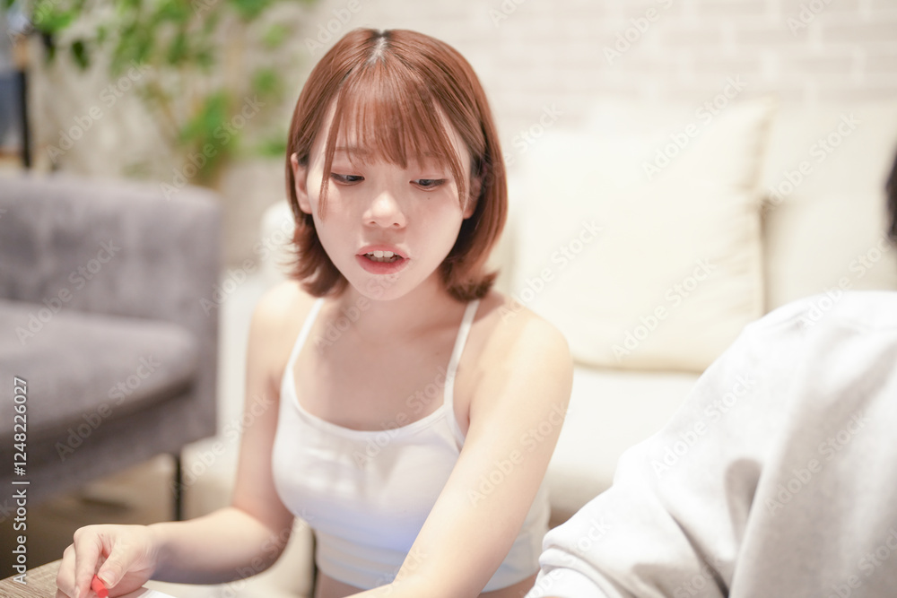 A Japanese pregnant woman in her 20s wearing clothes that show her stomach and her husband are sitting on a sofa in their apartment and drawing a picture of a New Year's celebration in 2025. A Japanese pregnant woman in her 20s wearing clothes that show her stomach and her husband are sitting on a sofa in their apartment and drawing a picture of a New Year's celebration in 2025.
