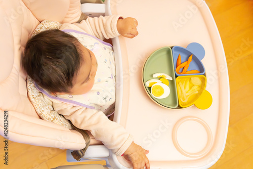 Billede på lærred baby sitting in feeding highchair with pink tray with colorful plate of healthy food cut into pieces