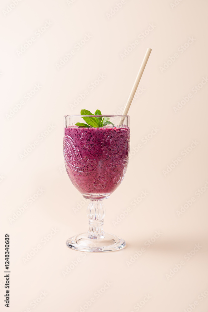Blueberry milkshake in cut crystal glass with beige straw and fresh mint on neutral background. Copy Space. Elegant and natural presentation. Concept of healthy eating, freshness and wellness Blueberry milkshake in cut crystal glass with beige straw and fresh mint on neutral background. Copy Space. Elegant and natural presentation. Concept of healthy eating, freshness and wellness