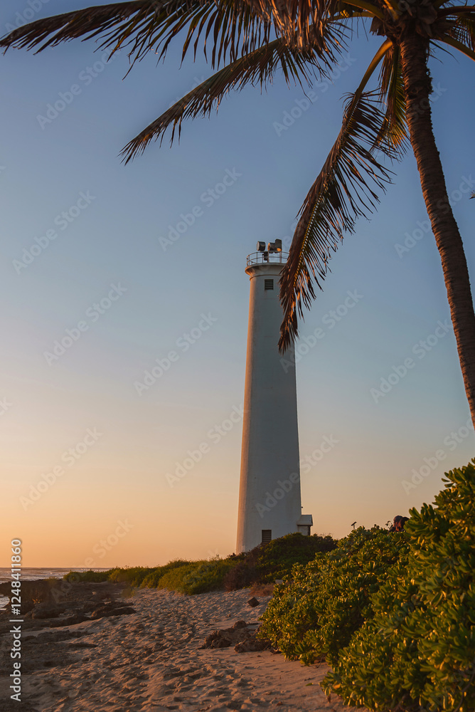 A tall white lighthouse stands near a sandy beach, surrounded by greenery and a palm tree, with the ocean partially visible under a golden sunset. A tall white lighthouse stands near a sandy beach, surrounded by greenery and a palm tree, with the ocean partially visible under a golden sunset.