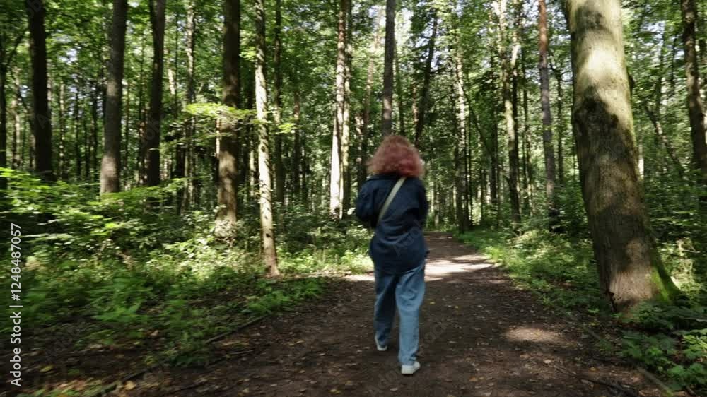 Woman walking in the forest, rear view from the back, engaging in leisure outdoor activity amidst natural greenery Woman walking in the forest, rear view from the back, engaging in leisure outdoor activity amidst natural greenery