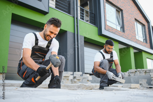 A group of multiracial workers lay paving stones on a sidewalk near a house photo