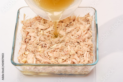 chicken broth is carefully poured in a thin stream into a square glass bowl with the future galantine photo