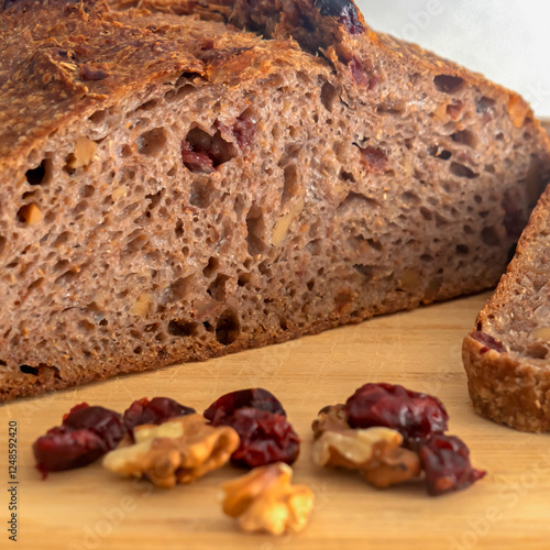 Pan de masa madre perfectamente horneado con nueces y arándanos, presentado sobre una tabla de madera / Perfectly baked sourdough bread with walnuts and cranberries, presented on a wooden board