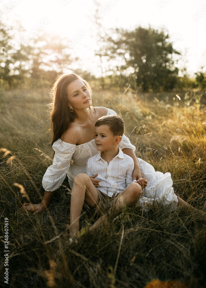 Fototapeta premium Mother and son sit in a golden meadow, in warm sunlight, sharing a quiet, thoughtful moment.