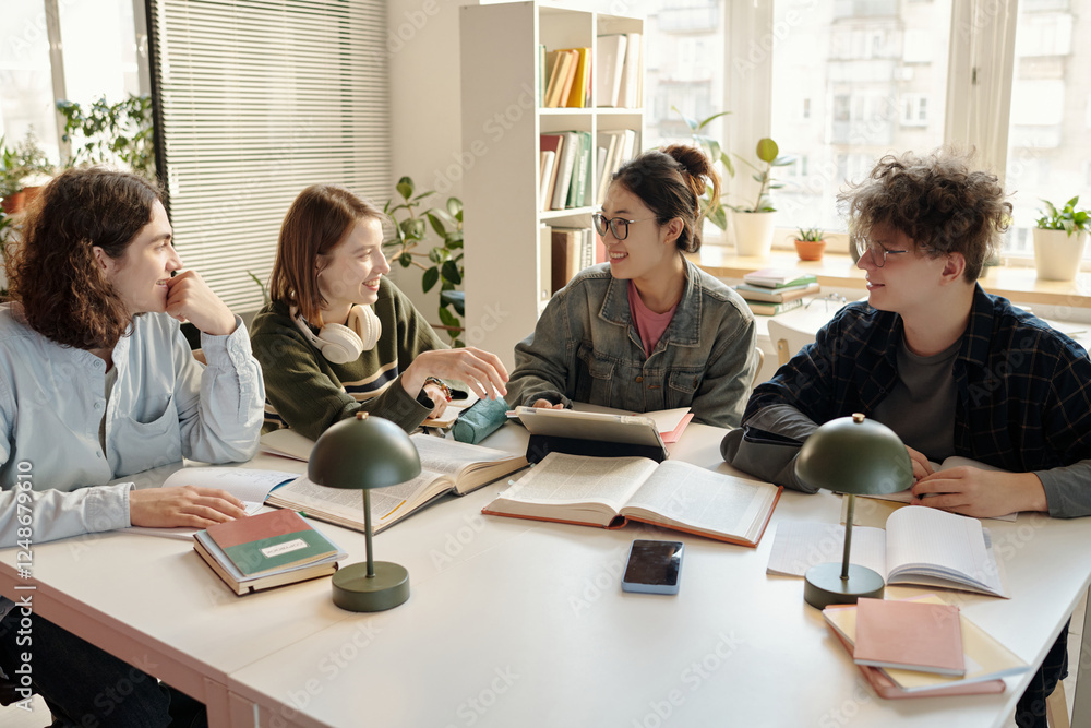Fototapeta premium Four young students collaborating together working in study group together sitting at desk in college library with books on table
