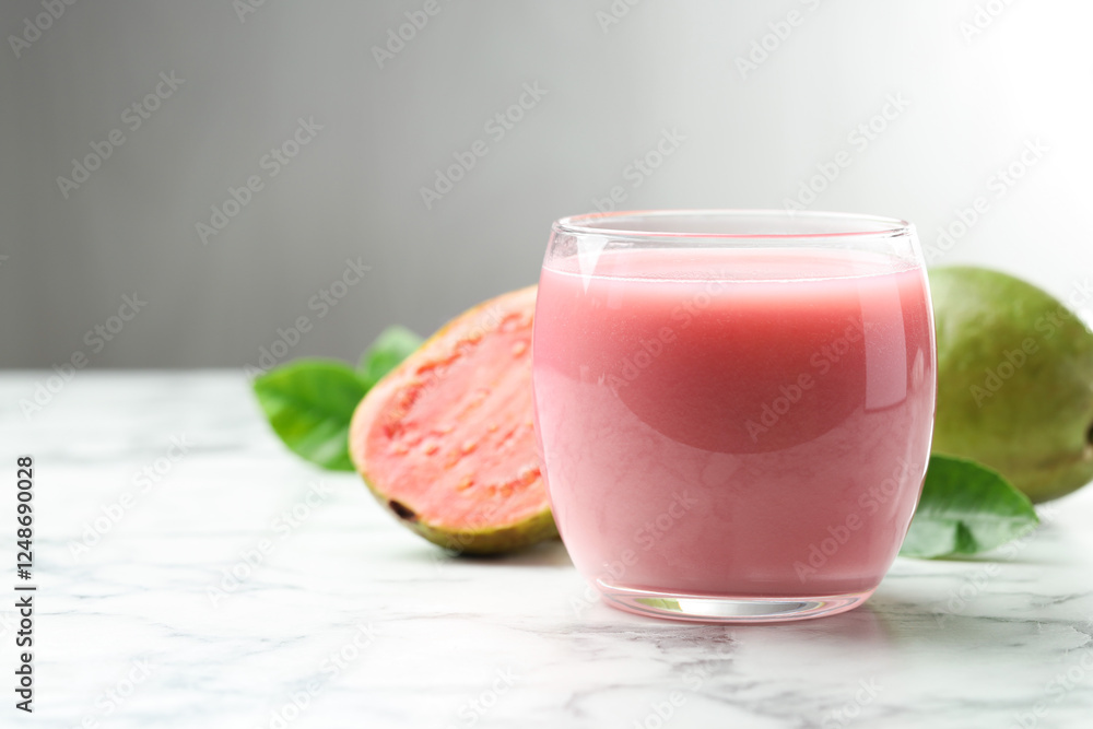 Tasty guava juice in glass, leaves and fruits on white marble table against grey background, closeup. Space for text Tasty guava juice in glass, leaves and fruits on white marble table against grey background, closeup. Space for text