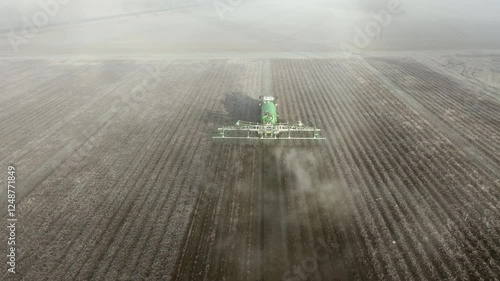 Tractor fertilizes a field in winter. Aerial drone video.