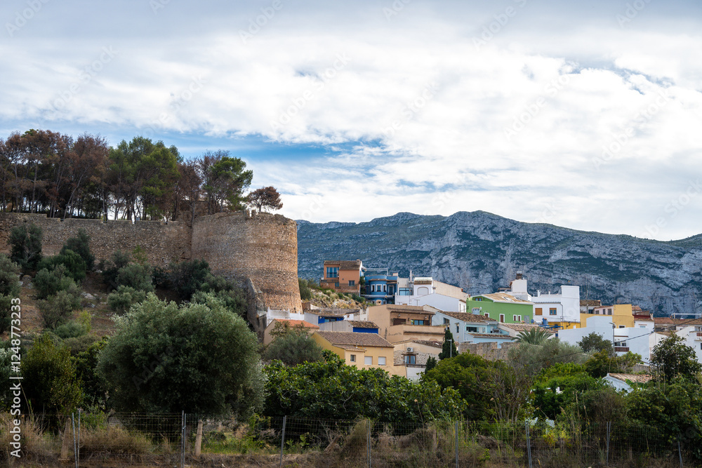 Ancient stone wall with a tower surrounded by lush greenery and colorful buildings Ancient stone wall with a tower surrounded by lush greenery and colorful buildings