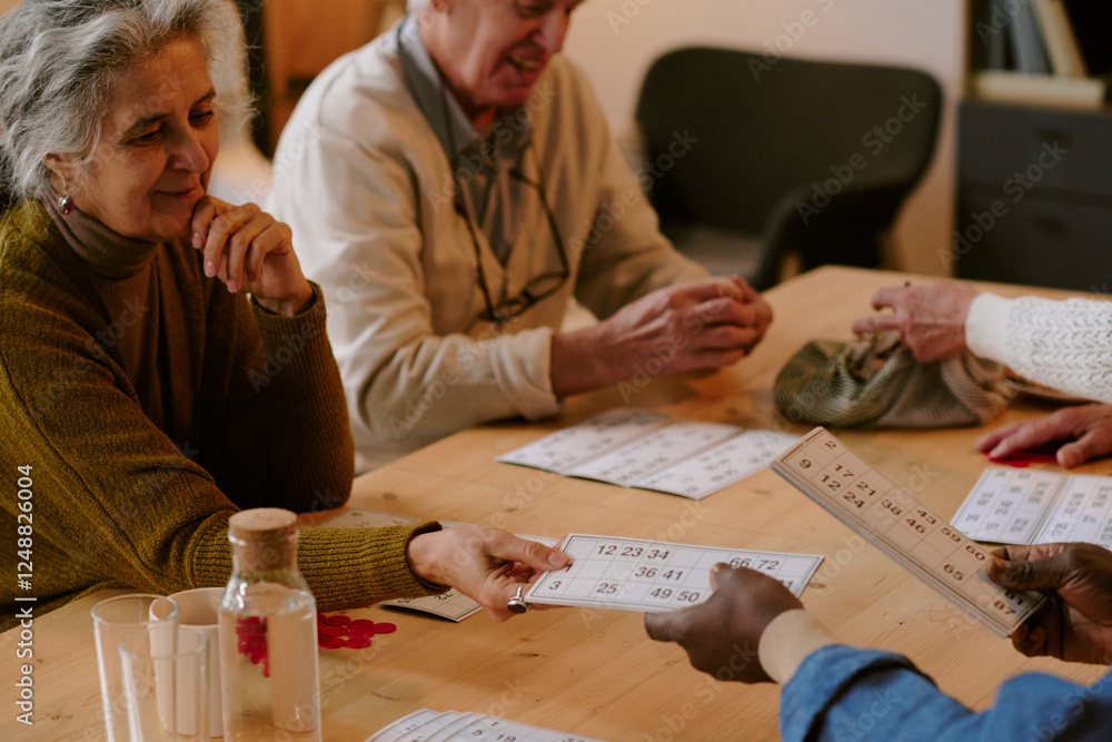 Obraz premium High angle shot of silver headed woman sitting at table and taking bingo card gently