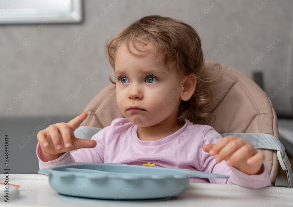 A serious toddler sitting at the table, observing her surroundings with focus in a cozy home setting A serious toddler sitting at the table, observing her surroundings with focus in a cozy home setting