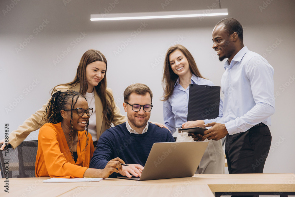 Professional team collaborating around laptop, displaying cultural diversity and teamwork in modern office environment