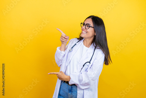 Young brunette doctor woman wearing stethoscope standing over isolated yellow background surprised and pointing her fingers side