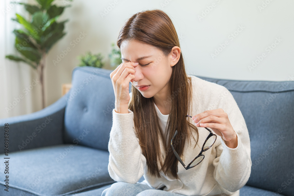 Eye care concept, fatigue asian young woman tired eyes irritated rubbing, massage nose ,eye dry relief vision pain sitting on couch, sofa at home, eye strain, hand holding glasses, suffer bad blurry. Eye care concept, fatigue asian young woman tired eyes irritated rubbing, massage nose ,eye dry relief vision pain sitting on couch, sofa at home, eye strain, hand holding glasses, suffer bad blurry.
