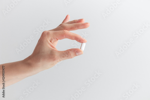 Female hand holding white pill with fingers on white background. Concept of health care, dietary supplements, treatment of depression and diseases. High-quality photo banner