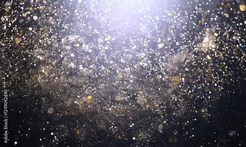 A close-up shot of a shower of golden glitter falling against a dark background. The glitter sparkles and shimmers as it falls, creating a magical and festive effect.