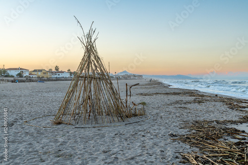 Pyramid-shaped bamboo structure on the beach at sunset with coastal houses photo