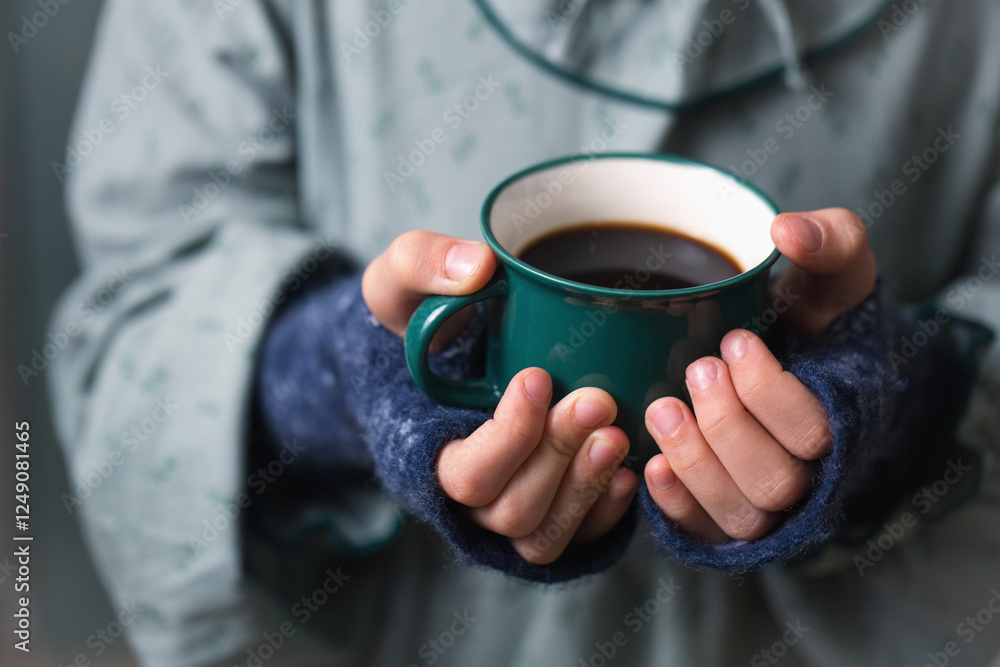 Children's hands in woolen mittens holding a green mug with a hot drink, copy space Children's hands in woolen mittens holding a green mug with a hot drink, copy space