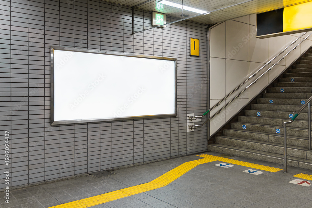 A blank billboard poster on a station wall next to an exit stairs. Space for text for advertising signage ideas and mockups
