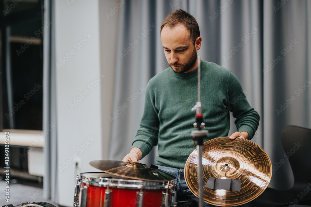 A man is intently practicing drums inside a music studio, focusing on the cymbals. The atmosphere is one of concentration and dedication, capturing the essence of music rehearsal. A man is intently practicing drums inside a music studio, focusing on the cymbals. The atmosphere is one of concentration and dedication, capturing the essence of music rehearsal.