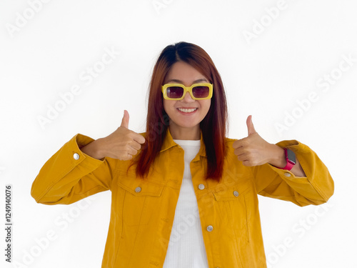 Happy asian Thai woman wear yellow jacket and sunglasses, showing thumbs up, recommend good and prefect, standing isolated over white background wall. photo