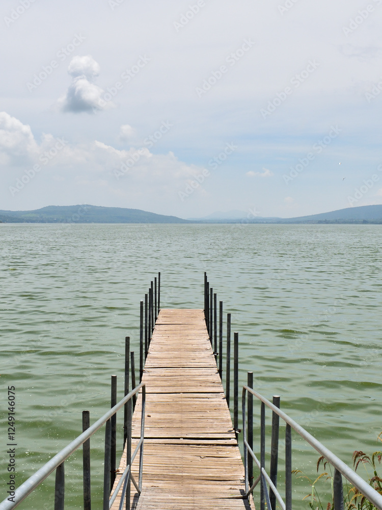 Obraz premium Cuexcomatitlan pier in the water, cloudy sky, in Cajititlan lake with a cloudy sky in the background. The water is green and calm
