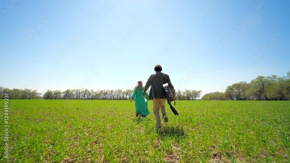 Couple running through green field in spring, man with guitar, wide-angle shot Couple running through green field in spring, man with guitar, wide-angle shot