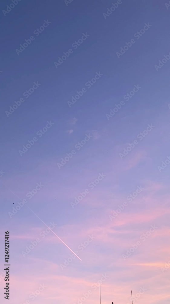 Jet contrail streaks through colorful evening sky with soft clouds in motion Jet contrail streaks through colorful evening sky with soft clouds in motion
