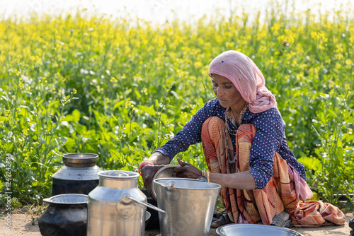 poor malnutrition village women living below poverty line washing dishes with mustard fields behind