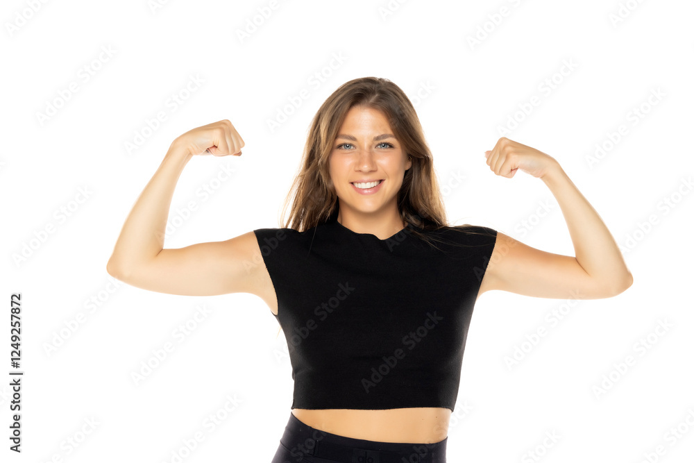 Woman in black crop top flexing both arms with joyful smile, showing strength and confidence on white background Woman in black crop top flexing both arms with joyful smile, showing strength and confidence on white background