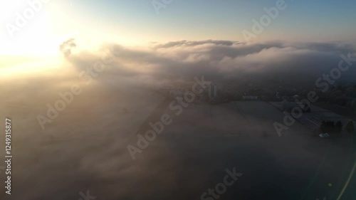 Aerial drone footage of sideways flight over countryside and outskirts of a city during foggy sunrise