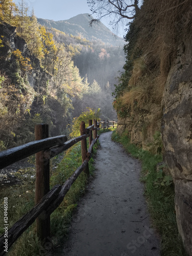 Scenic mountain pathway winding through rocky terrain, wooden fencing framing autumn landscape with distant peaks in soft golden light Isollaz waterfall photo