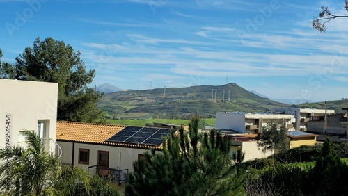 Wallpaper Mural Scenic view of green hills with wind power plants against the blue sky. in the foreground are modern houses with solar panels Torontodigital.ca