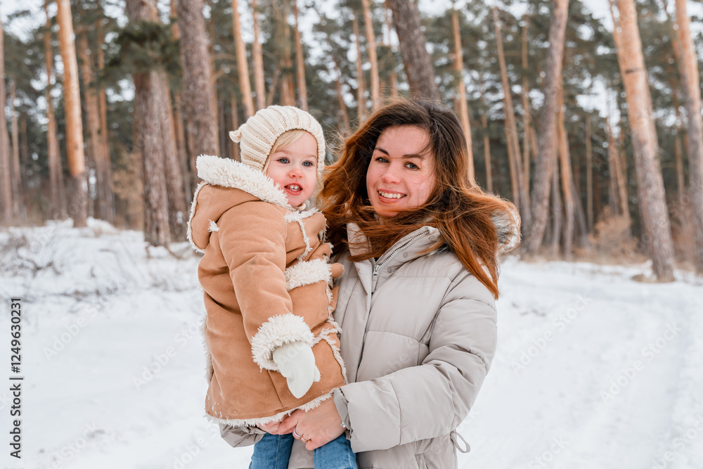 Fototapeta premium A mother with her little child daughter in a snowy winter forest.