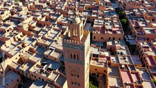 Explore the vibrant rooftops of Marrakech filled with traditional architecture and bustling life. The historic Koutoubia Mosque stands tall amidst the colorful homes under a clear sky.