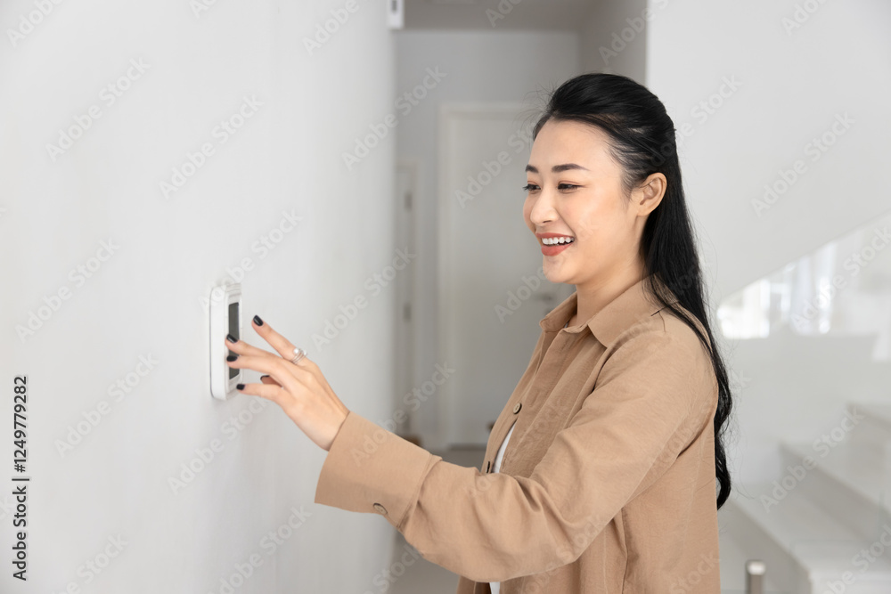 Happy young Asian homeowner woman typing on wall mounted climate control panel, regulating temperature at home, starting air conditioner in apartment, pushing button on device, smiling Happy young Asian homeowner woman typing on wall mounted climate control panel, regulating temperature at home, starting air conditioner in apartment, pushing button on device, smiling
