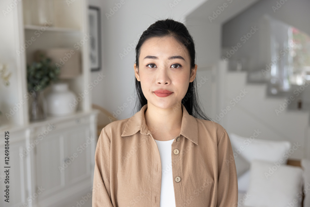 Serious beautiful young Vietnamese woman in casual posing for head shot, standing in white colored cozy home interior, looking at camera. Female Asian model front video call screen portrait Serious beautiful young Vietnamese woman in casual posing for head shot, standing in white colored cozy home interior, looking at camera. Female Asian model front video call screen portrait