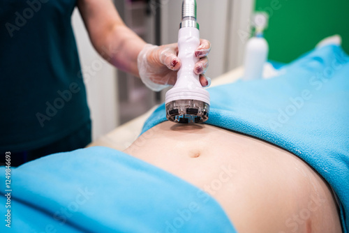 Professional dermatologist performing radio frequency lifting procedure on the stomach of a woman. Female client getting rf-lifting treatment on her belly at cosmetology clinic