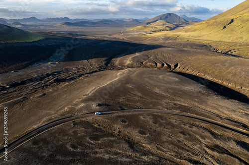 Aerial perspective of a car navigating a sparse basalt road Landmannalaugar in Iceland, surrounded by barren landscapes and bathed in warm sunlight