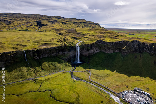 A magnificent aerial view Seljalandsfoss waterfall in Iceland plunges over the edge of green cliffs, surrounded by stunning countryside. The serene landscape captures beauty of untouched nature