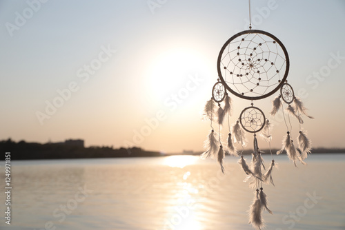 Beautiful handmade dream catcher near river at sunset. Space for text photo