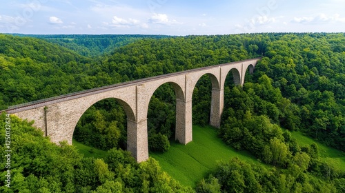 A stunning stone viaduct arches gracefully over lush green forests, showcasing a blend of nature and engineering in a serene landscape. photo