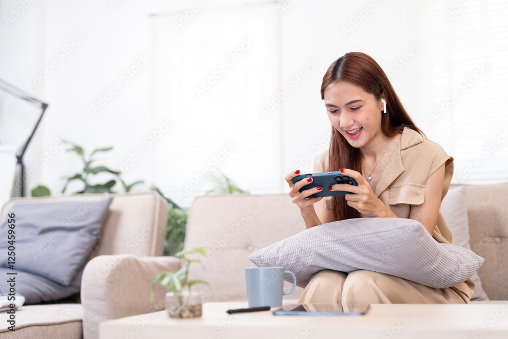 Excited young Asian woman sitting on couch in living room, playing mobile game or watching movie on smartphone Excited young Asian woman sitting on couch in living room, playing mobile game or watching movie on smartphone