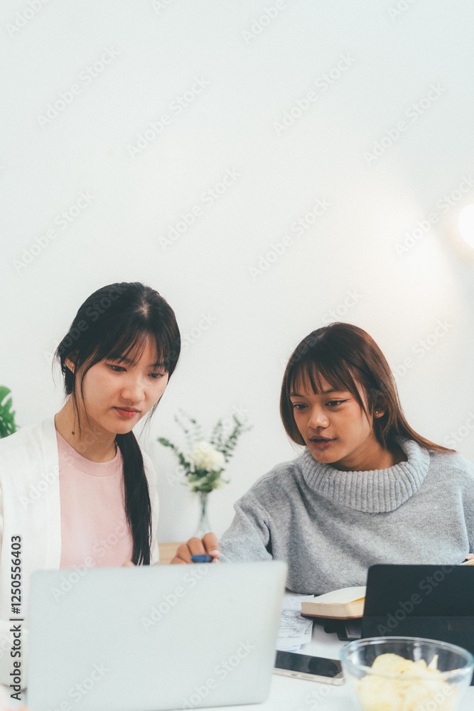 Female higher education student using laptop and studying book in home, Online learning.