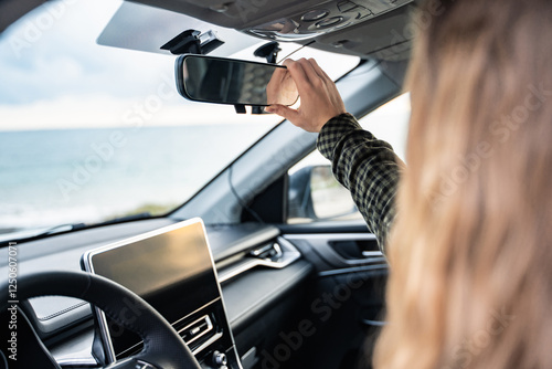 Backside view of an unrecognizable woman adjusting the rearview mirror in her car before driving. Female driver following safe ride rules. Ready for travel with automobile. Safety first. Inside auto.